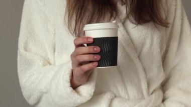 Woman in a bathrobe holding a cup of morning coffee.