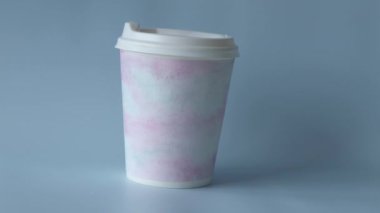 Plastic coffee cup with delicate watercolor pattern on blue background. Woman picks up coffee.