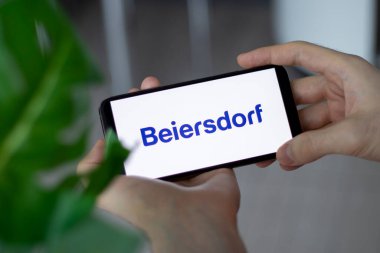 IRPEN, UKRAINE - 20 HAZİRAN 20223, akıllı telefon ekranı Beiersdorf logosu kapanışı erkek ellerinde, Illustrative Editorial