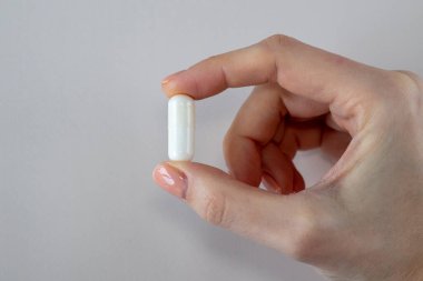 Beyaz arka planda beyaz bir arka plan üzerinde kadın eli olan büyük beyaz bir kapsül. Haplar, ilaçlar ve vitaminler.