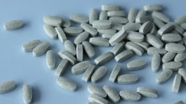 Vitamin takviyeleri, mikro besin kompleksi. Mavi arka planda dalgalanmalar olan oval tabletler. Kameranın soldan sağa hareketi