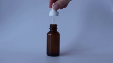 Kadın siyah bir şişeyi damlatıcıyla açıyor ve ürünü damlatıyor. Cilt bakımı için yağ ya da serum