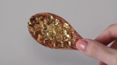 D3 vitamini takviye kapsülleri, beyaz arka planda, bir kadının elinde, tahta kaşıkta. Haplar, ilaçlar ve vitaminler. Yakın plan.
