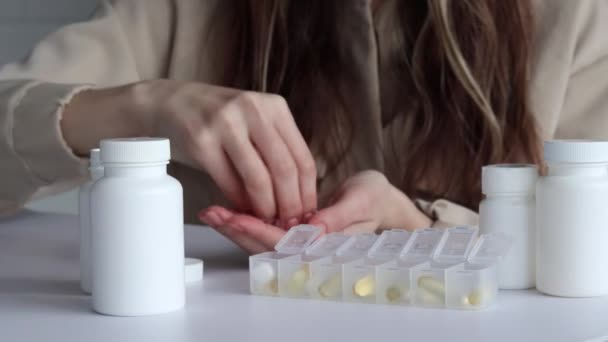 女性は丸いカプセルを錠剤容器に1週間広げます 白いモックアップ瓶が前景にあります — ストック動画