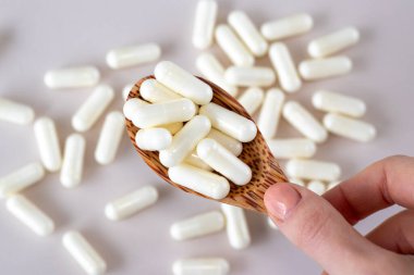 Beyaz C vitamini kapsülleri, tahtadan bir kaşıkta bej bir arka planda dağınık ilaçlarla.