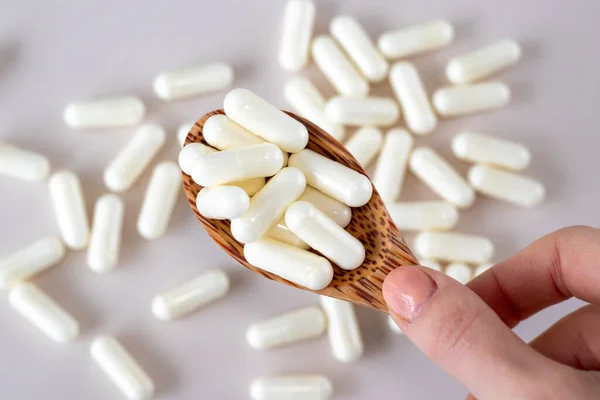 Beyaz C vitamini kapsülleri, tahtadan bir kaşıkta bej bir arka planda dağınık ilaçlarla.
