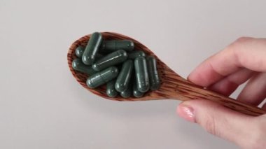 Klorofil ya da spiral içeren yeşil kapsüller. Beyaz arka planda tahta bir kaşıkta işe yarar takviyeler ya da ilaçlar. Yakın plan.