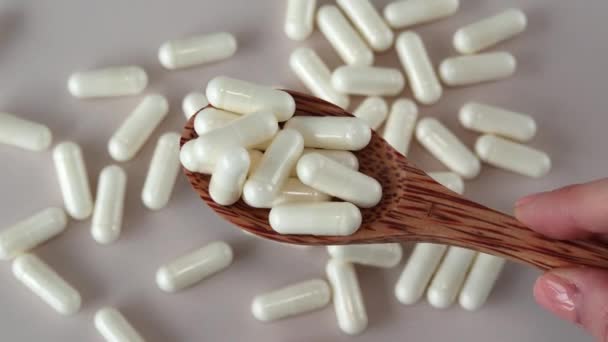 散乱薬とベージュの背景に木製のスプーンで白いビタミンCカプセル — ストック動画