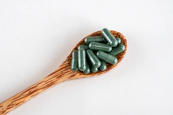 stock image Green capsules with spirulina or chlorella supplements in a wooden spoon, top view. Dietary supplements