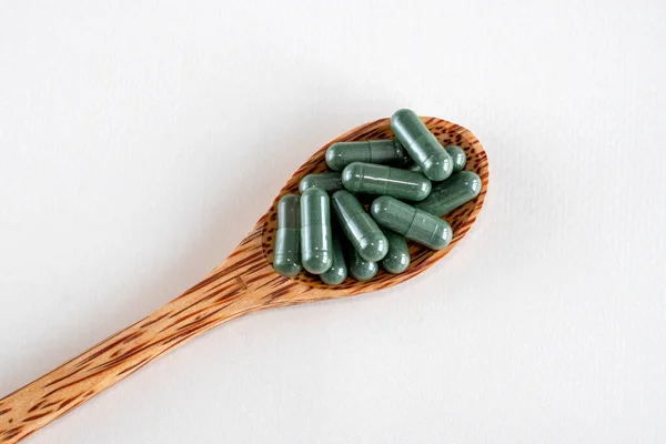 Stock image Green capsules with spirulina or chlorella supplements in a wooden spoon, top view. Dietary supplements