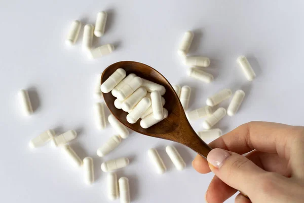 stock image Lots of pills on a white background in a wooden spoon. Nutritional supplements with enzymes, vitamins, medications or pills