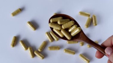 İçinde sarı-bej tozu olan şeffaf kapsüller. Karaciğer sağlığı için bir ilave ya da tablet. Beyaz bir geçmişi ve dağınık ilaçları olan bir kaşık dolusu ilaç.