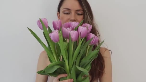 白い背景にピンクのチューリップの花の花束で笑顔の美しい幸せな若い女性 女の子は花の匂いがする — ストック動画