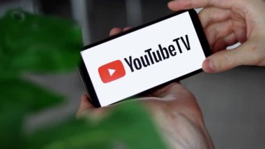 IRPEN, UKRAINE - JANUARY 20 20223, Closeup of smartphone screen YouTube TV logo lettering with in mans hands, Illustrative Editorial