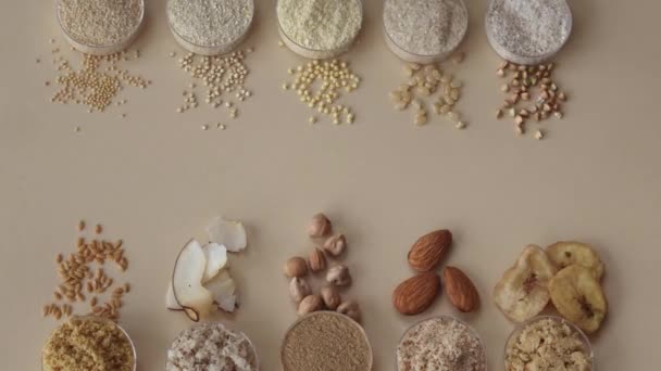 様々なグルテンフリーの小麦粉 ひよこ豆 緑のそば アーモンド ココナッツ バナナ アマランス ベージュの背景にキノア スペースのコピーを持つトップビュー — ストック動画