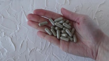 Bir kadının elindeki gri bitkisel kapsüller yakın plan..