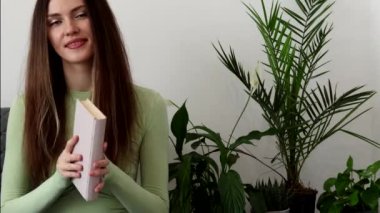 Uzun saçlı ve elinde kitap tutan mutlu, güzel bir genç kadın. Fotoğraftaki yeşil tonlar.