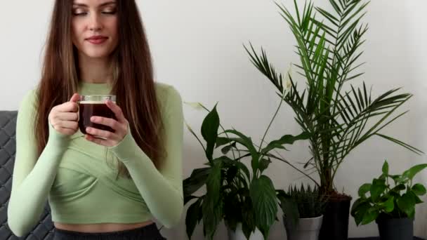 Красивая Молодая Женщина Наслаждается Ароматом Кофе Белом Фоне Зелеными Растениями — стоковое видео
