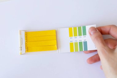 Bir kadın elinin beyaz arka planında Ph 'yi ölçmek için test şeritleri.