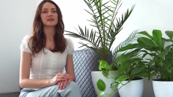 Vacker Ung Kvinna Sitter Soffan Bredvid Rummets Växter Och Gratulerar — Stockvideo