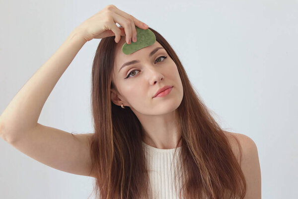 Крупный план портрета красивой девушки с рыжими волосами, массирующей лицо каменным скребком.