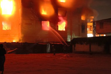 İtfaiyecilerin siluetleri gece vakti şehrin içinde hortumla yangını söndürüyor.
