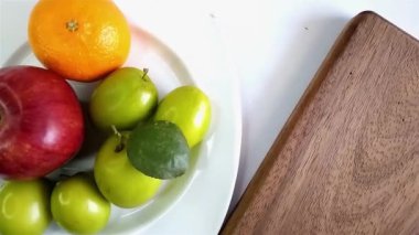 Beyaz bir tabakta elma, mandalina ve taze yeşil meyve gibi çeşitli meyvelerin üst görüntüsü..