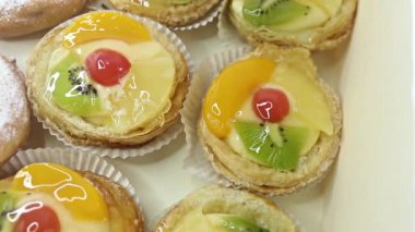 Lezzetli Danimarka meyveli tartlar ve çörekler bir kutuda. Kremalı hamur işleri, bir dilim kivi, ananas, mandalina ve kiraz..