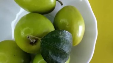 Olgun yeşil jujube meyvesinin üst görüntüsü beyaz bir tabakta, sarı arka planda. Dönen Hint jujube ziziphus mauritiana meyve kavramı.