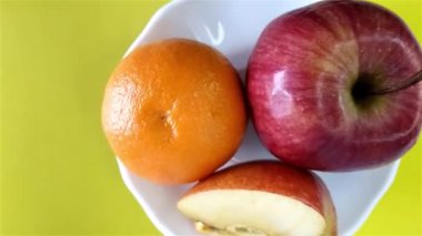 Olgun, lezzetli, dilimlenmiş ve sarı arka planda dönen beyaz tabakta elma ve mandalinanın üst görüntüsü. Sağlıklı gıda konsepti.