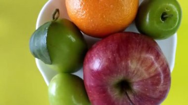 Olgun elma, meyve suyu ve mandalinanın üst görüntüsü sarı arka planda dönen beyaz tabakta. Sağlıklı gıda afişi.