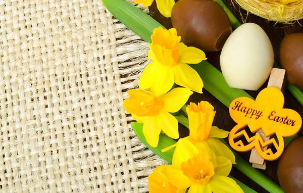 Easter composition. Narcissus flower and easter chocolate eggs on burlap background.