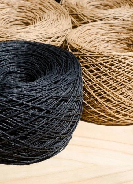 stock image Raffia balls close-up on a wooden board. Skeins of black and beige raffia are ready for knitting.