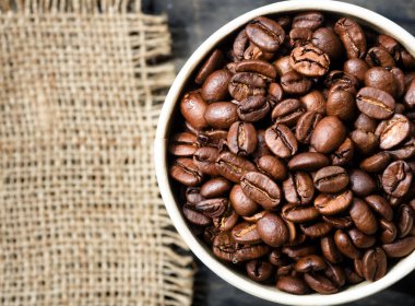 Coffee beans in a paper cup. Burlap in blur, space for text. Grains of a tropical plant.