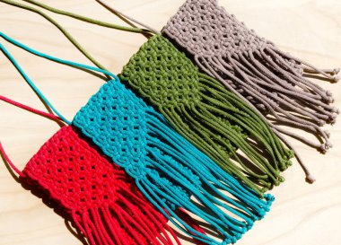 Makrome tekniğiyle örülmüş küçük çantalar. Ahşap bir arka planda çok renkli cep telefonu çantaları.