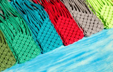 Küçük çantalar makrome tekniği kullanılarak tığ işi yapılır. Turkuaz arka planda cep telefonları için çok renkli çantalar..