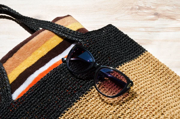 stock image Black raffia beach bag. Women's bag with a towel and sunglasses on the table.