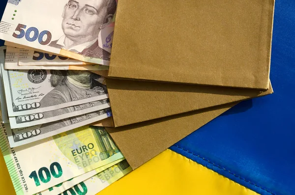 Money in an envelope on the Ukrainian flag. Hryvnia currency, dollars and euros. Assistance to Ukraine from countries in connection with the military aggression of Russia.