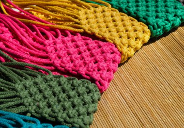 Bambu arka planında makrome tekniğiyle örülmüş küçük el çantaları. Cep telefonları için çok renkli çantalar.