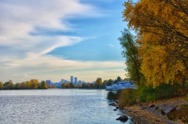 Kyiv 'in Obolonsky bölgesinde güzel bir sonbahar manzarası. Dinyeper nehrinin kıyısındaki sarı ağaçlara karşı mavi bulutlar..