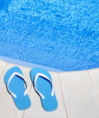 Flip flops on the background of the pool. Blue slippers lie near the blue water.