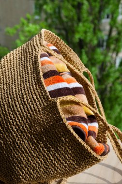 Renkli havluyla birlikte rafya 'da bir plaj çantası. Yeşil ağaçların arka planında duran kadın çantası. Hobi, dikiş işi..