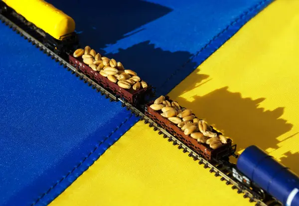 Against the background of the Ukrainian flag is a model of a railway with fuel tanks and wagons with wheat. Model train on the Ukrainian flag.