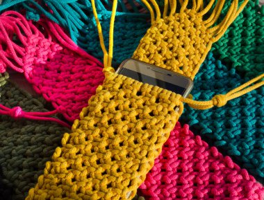 Pamuk ipindeki makrome tekniğini kullanarak örülmüş küçük torbalar. Ahşap arka planda cep telefonları için çok renkli çantalar..