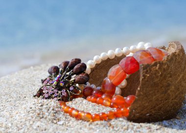 Okyanus kıyısında hazineler. Mavi okyanusun arka planında kumda inci, kehribar ve mücevher..