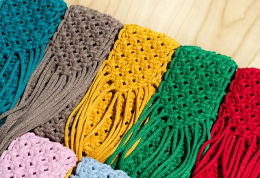 Makrome tekniğiyle örülmüş küçük çantalar. Ahşap bir arka planda çok renkli cep telefonu çantaları.