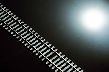 Toy railway and sun on glossy black background. Railway line. Selective focus effect. Rails and sleepers on dark background clipart