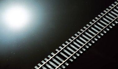 Toy railway and sun on glossy black background. Railway line. Selective focus effect. Rails and sleepers on dark background clipart