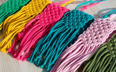 Makrome tekniğiyle örülmüş küçük çantalar. Ahşap bir arka planda çok renkli cep telefonu çantaları.