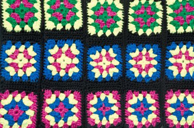 Pembe, beyaz, mavi ve yeşil renkli büyükanne kare merkezli siyah karelerin yer aldığı canlı bir pamuk örgü projesi.